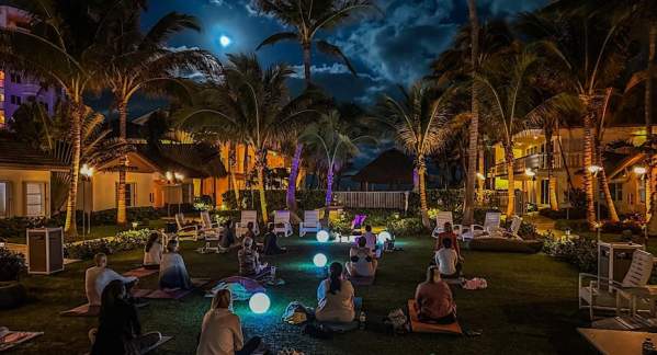 A groupmeditating under a full moon in a grassy courtyard at the Beachcomber Resort and Club. Colorful orbs are interspersed throughout the group