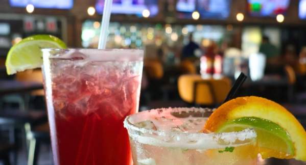 Two Cocktails sitting on a table with four TV screens in the background