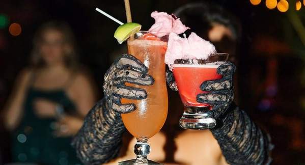 Two drinks, being held up by two hands gloved in black lace.