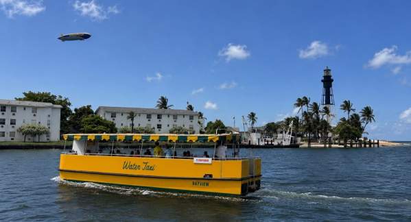 The Pompano Beach Water Taxi in the Hillsboro Inlet, with the GoodYear Blimp in the sky and the Hillsboro Lighthouse in the background.