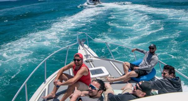 Five guys sitting on the bow of a fishing boat heading out to go fishing in beautifully clear blue waters off Pompano Beach.