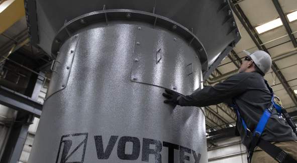 A worker inside a shop touching a piece of equipment with the name "Vortex" on it.