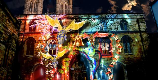 Exchequer Gate at night with a light display projected onto its front, with Lincoln Cathedral in the background