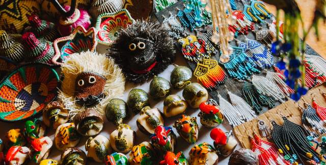 Indigenous Panamanian crafts, featuring hand-painted animal figurines, yarn dolls, colorful beaded necklaces and bracelets, and woven baskets, all arranged on a table.