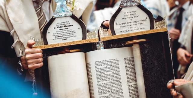 A close-up shot of a Torah scroll, its wooden rollers visible, being carefully carried by a rabbi in a traditional black caftan, in a synagogue