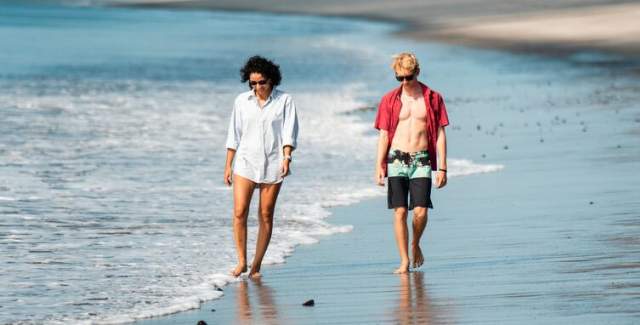A pair of buddies take a leisurely walk by the shore of the beach.
