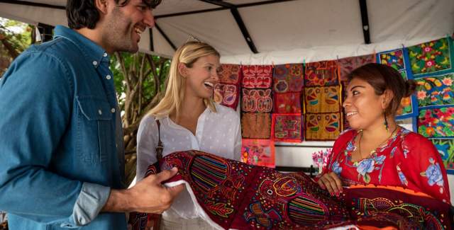Mujer de la comunidad muestra una Mola tradicional a un par de visitantes.