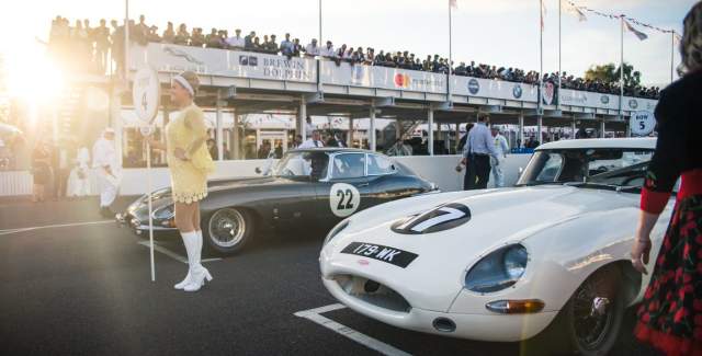 Two cars on the start line at the vintage car festival with crowds in pit lane and grandstand, Goodwood Revival