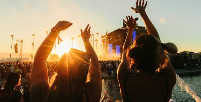 two people silhouetted with their arms up at a festival, the stage is in the distance