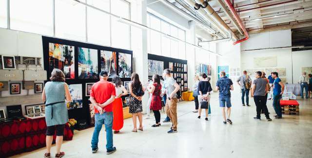an image of a large warehouse style room with art displayed with multiple people walking around