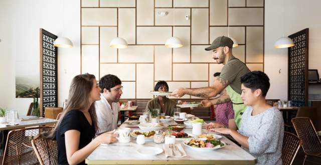 Man Serving Food To 3 People At A Table In Laziz Kitchen