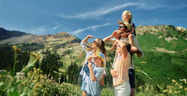 Family on a mountain trail all shading their eyes and looking at something in the distance with mountains in the background
