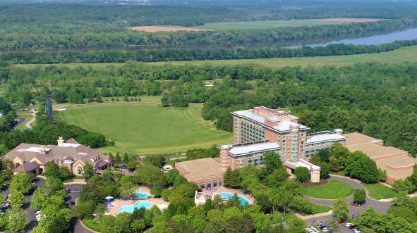 Aerial view of a Lansdown Resort in Leesburg, Virginia with lush green landscapes, a river in the background and outdoor pools surrounded by trees and golf courses.