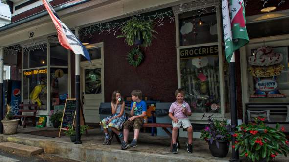 Three children eating hand-dipped ice cream cones on a bench outside Round Hill Farm to Trail Co in Loudoun