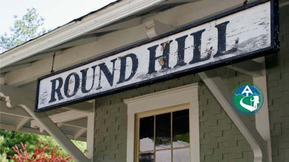 Weathered Round Hill sign on the historic train station, with the Appalachian Trail Community designation badge