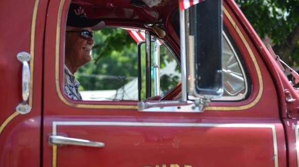 Smiling driver of a vintage red fire truck with an American flag during a Fourth of July parade in Loudoun County