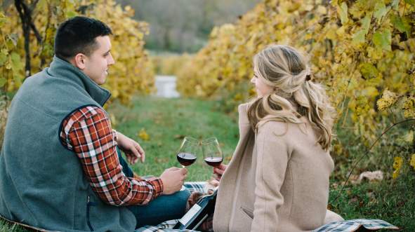 Couple drinking wine while sitting on the ground between in the vines of Bluemont Vineyard