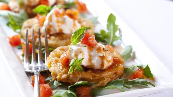 A close-up of a gourmet dish, from Tuscarora Mill in Downtown Leesburg, Virginia, featuring fried patties topped with creamy sauce and diced tomatoes on a bed of arugula.