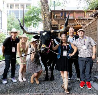 Group of people wearing cowboy hats and smiling at the camera while standing with a Longhorn.