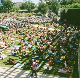A large group of people sitting on a green lawn in front of a stage for the Austin Blues Festival.