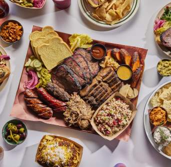 Colorful plates and trays of LeRoy and Lewis Barbecue, including sausage, brisket, frito chili pie, chips and crudite and more.