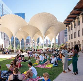 Groups of people standing around and sitting on picnic blankets across the Blanton Museum's lawn, in between museum buildings.