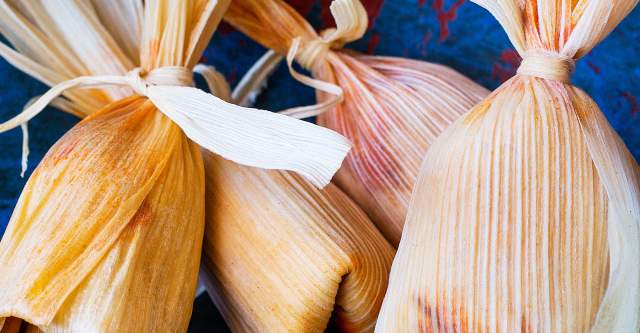 Corn husk wrapped New Mexican Tamales sitting on a colorful tablecloth