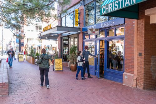 A couple walks into Liberty Puzzles on Pearl Street with Postino Wine Bar in the background