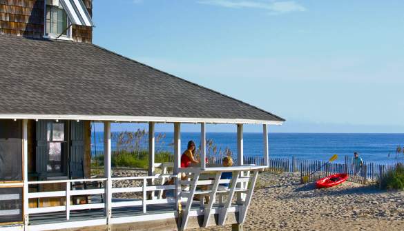 Visitors enjoy the fresh air and view from the wrap-around porch of their Outer Banks vacation rental.