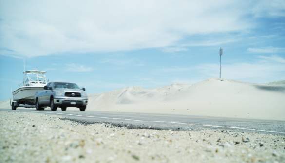 A truck with a boat on a trailer travels along Highway 12 of the Outer Banks in NC