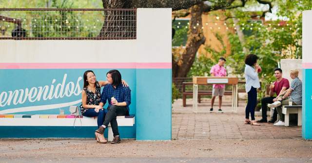 Couple sitting in front of Bienvenidos sign under live oak tree at Fresas outdoor patio in Austin Texas