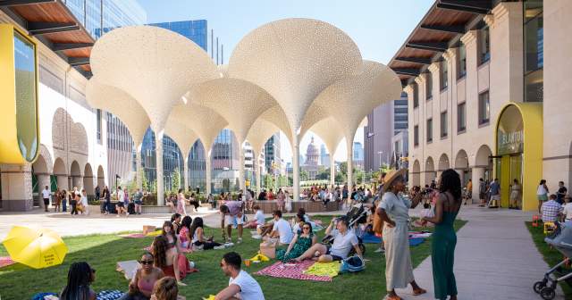 Groups of people standing around and sitting on picnic blankets across the Blanton Museum's lawn, in between museum buildings.