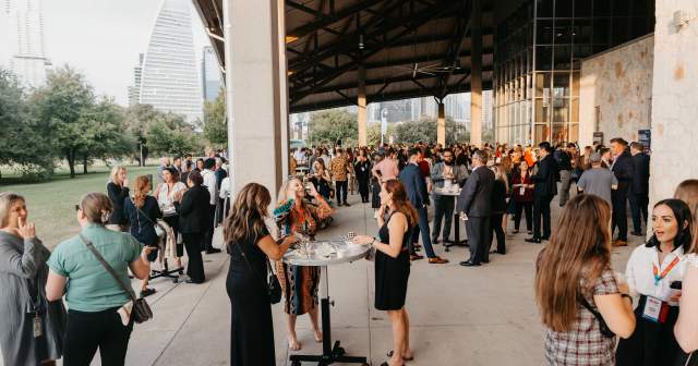 People with event badges on standing under the pavilion at Palmer Events Center during golden hour.
