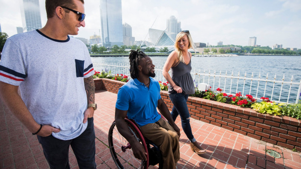 Three friends, including one using a wheelchair, wander along Milwaukee’s lakefront with the skyline in view.