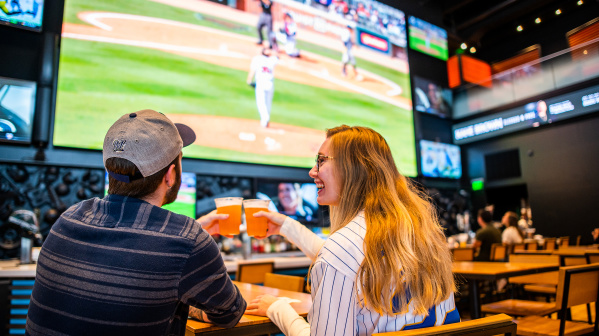 couple cheersing beer at bar with baseball on tv