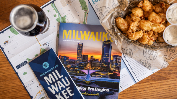 The 2026 Milwaukee Official Visitors Guide and Official Visitors Map are displayed with a beer and cheese curds on a table.