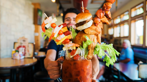 bartender showing huge bloody mary with burger and other food