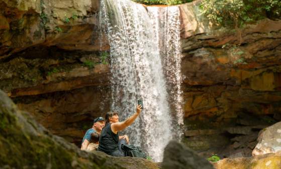 A family takes a selfie in front of a waterfall.