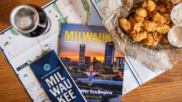 The 2026 Milwaukee Official Visitors Guide and Official Visitors Map are displayed with a beer and cheese curds on a table.