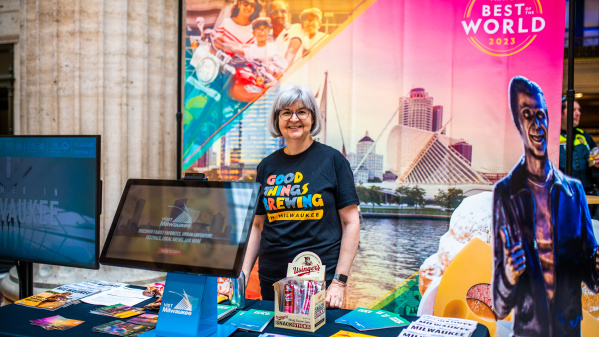 smiling volunteer stands by Visit Milwaukee display at union station