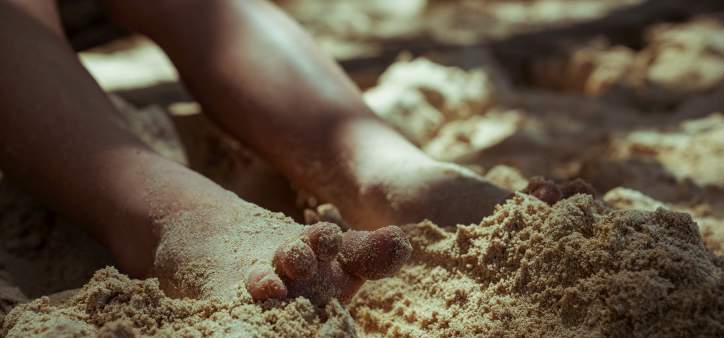Close up picture of two feet buried in the sand on a beach in Jamaica