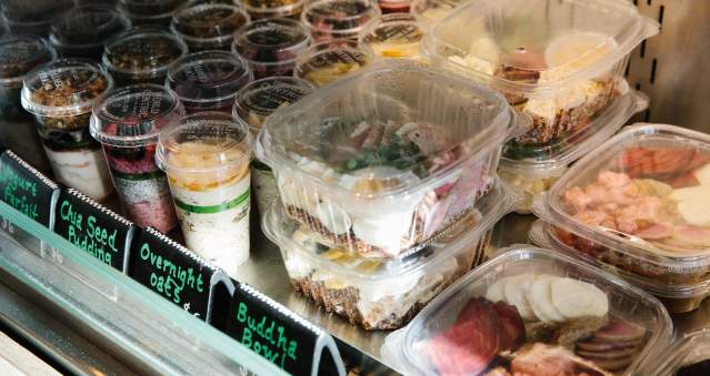 A display of assorted pre-packaged meals in clear containers, including overnight oats, chia seed pudding, and Buddha bowls, in a refrigerated case.