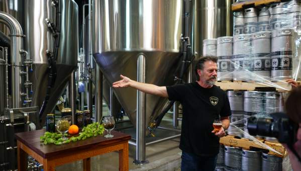 A man giving a tour of a brewery, surrounded by industrial brewing equipment