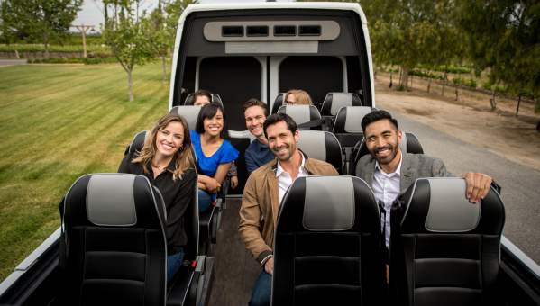 A group of people riding in a roofless van through a vineyard