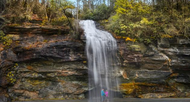 Man and Woman standing behind Bridal Veil Falls in Highlands, North Carolina.