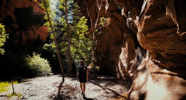 A man hikes through a red rock slot canyon in Southern Utah