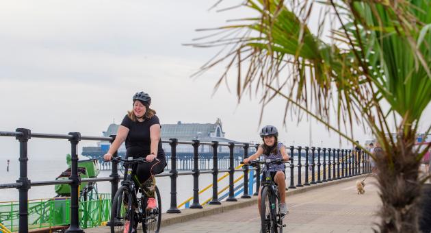 Mother and daughter cycling near the seafront with a pier in the background