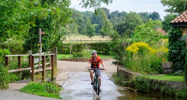 Man cycling through puddle in rural village