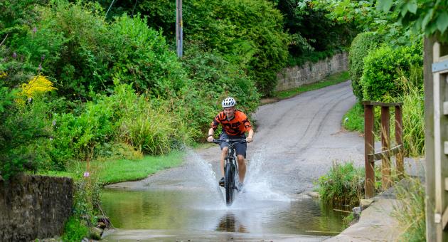 A man cycling through a large puddle in a village