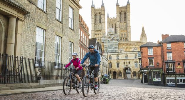 A man and woman cycling in front of Lincoln Cathedral
